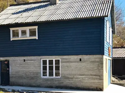 a man standing in the doorway of a blue house at 9 person holiday home in Reksteren in Haukafer