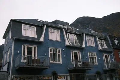 a blue house with white windows and mountains in the background at Blue House Dormitory in Odda