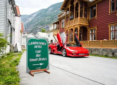a red car parked next to a sign in front of a house at Lærdalsøren Motor Guesthouse in Lærdalsøyri