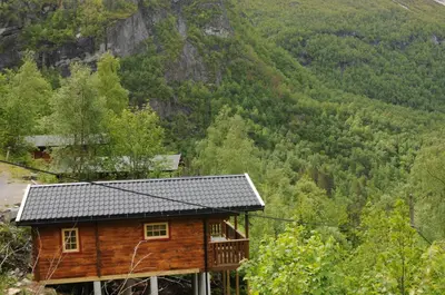 a wooden cabin with a mountain in the background at Fossen Accommodation in Geiranger