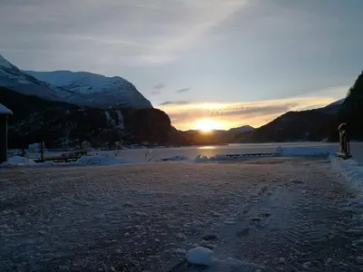 a sunset on a beach with snow covered mountains at Old School på Eidslandet - exclusive apartment in Eidslandet