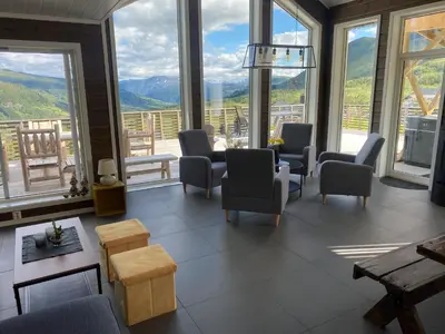 a living room with chairs and tables and windows at Pudderhytta in Sogndal