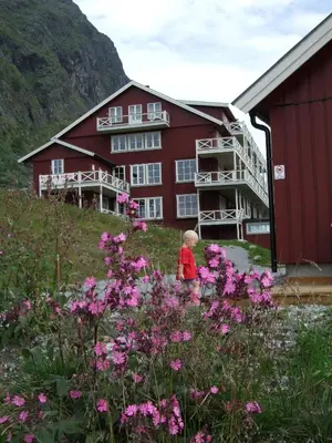 a child standing in front of a red building with flowers at Nystuen in Tyinkrysset