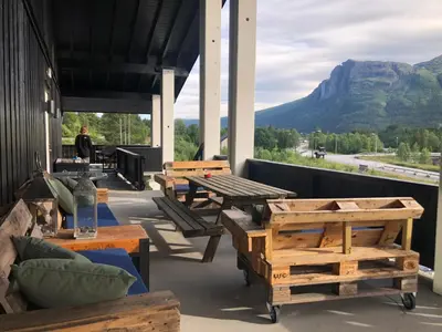 a patio with wooden tables and benches and a mountain at Storehorn Apartments Hemsedal in Hemsedal