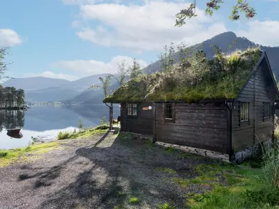 an old cabin with a grass roof next to a lake at Holiday Home Strandbu by Interhome in Viksdalen