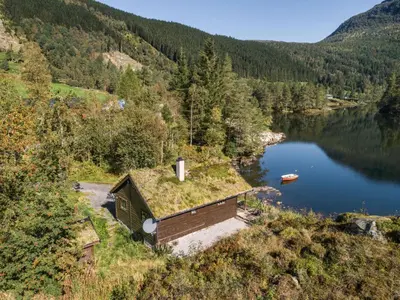 a building with grass on the roof next to a lake at Holiday Home Strandbu by Interhome in Viksdalen