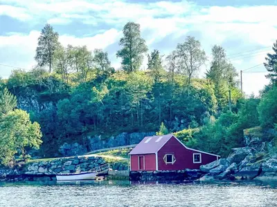 a red house on the water next to a boat at Holiday Home Bjørkeneset by Interhome in Uggdal