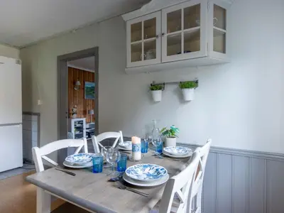 a wooden table with white chairs and a kitchen at Chalet Gulehuset by Interhome in Gjelland