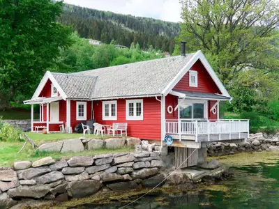 a red house on the water with a stone wall at Chalet Naustet by Interhome in Balestrand
