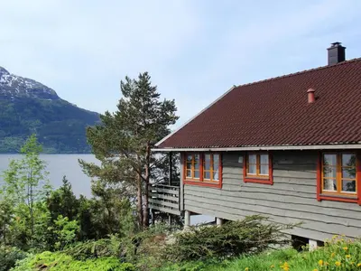 a house with orange windows and a lake at Chalet Eiknes by Interhome in Tjoflot