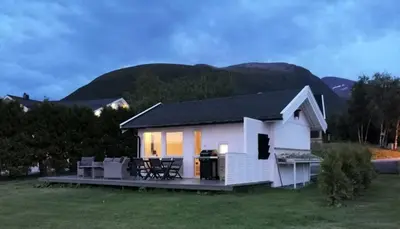 a small white house with mountains in the background at feriehus ved sjøen in Tomrefjord