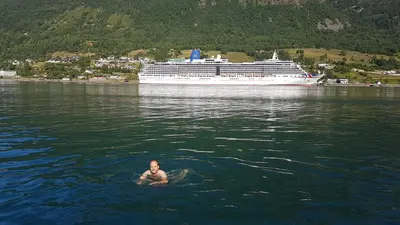 a man swimming in the water with a cruise ship at Nesset Fjordcamping in Olden