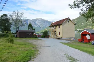 a house on a road with mountains in the background at Nesset Fjordcamping in Olden