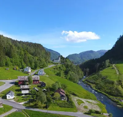 a village in the mountains with a river at Eidegrend Boutique Hotel in Eikelandsosen