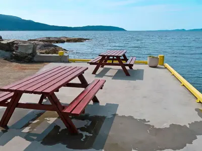 two picnic tables sitting next to a body of water at Holiday Home Nesholmen by Interhome in Leirvik