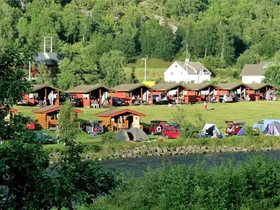 a group of lodges in a field next to a river at Lunde Camping in Aurland