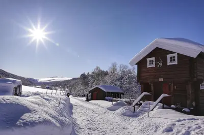 a log cabin in the snow with the sun behind it at Rondane River Lodge - Rondane Gjestegård in Enden