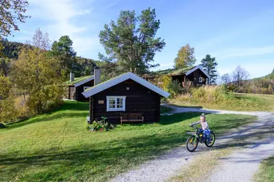 a girl riding a bike in front of a cabin at Rondane River Lodge - Rondane Gjestegård in Enden
