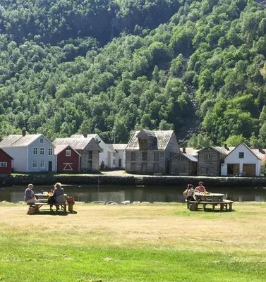 a group of people sitting on picnic tables near a body of water at Old town boutiqe apartments/ Gamle Lærdalsøyri boutique leiligheter in Lærdalsøyri