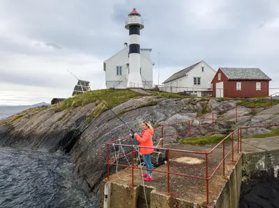 a woman standing on a pier near a lighthouse at Flatflesa Fyr - by Classic Norway Hotels in Rindarøy