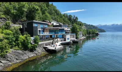 a building on the side of a river with boats at Panoramaresort in Hardangerfjorden leilighet i sjøkanten ved Hardangerfjorden for 7 personer boat , sauna,kajak, SUP for rent in Øystese