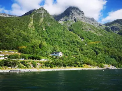 a house on the side of a mountain next to the water at Iris Vedal in Nauste