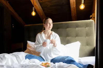 a woman sitting on a bed holding a cup of food at Jølstraholmen Landskapshotell in Vassenden