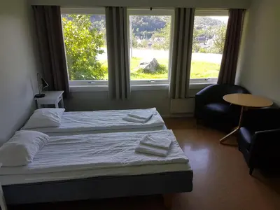 a bedroom with a bed and a chair and two windows at Folgefonn Gjestetun in Jondal