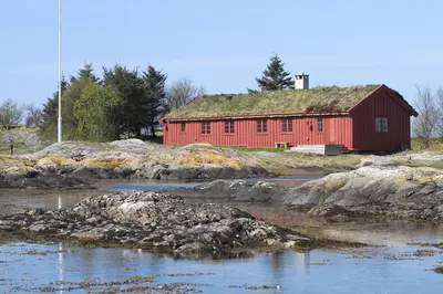 a red barn with a grass roof next to a river at Korsholmen - by Classic Norway Hotels in Karvåg