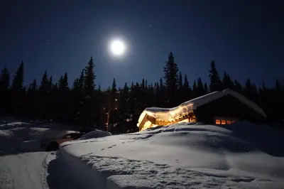 a house covered in snow at night with the moon at Liaplassen Mountain View in Beitostøl