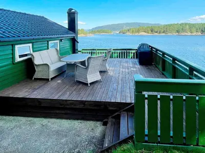a wooden deck with chairs and a table on the water at 6 person holiday home in LINDÅS in Lindås