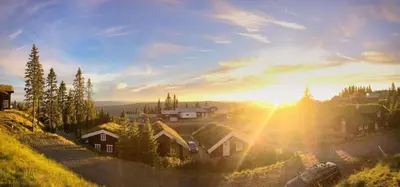 a village on a hill with the sun setting at Large family cabin in Hafjell ski in-out, BBQ, terrace and fireplace in Hafjell