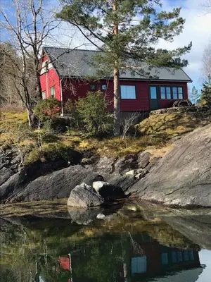 a red house on top of a hill next to the water at Teigen Leirstad, feriehus og hytter in Eikefjord