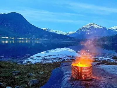 a bonfire on the shore of a lake with mountains at 8 person holiday home in Austefjorden in Austefjorden