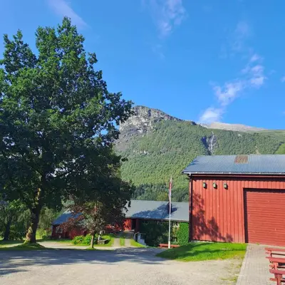 a red building with a tree and a mountain at Lensmansgarden in Innfjorden
