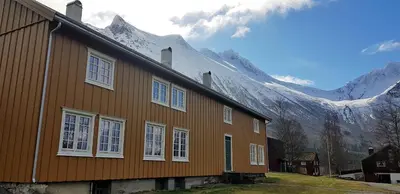 a brown house with mountains in the background at Lensmansgarden Marteinsgarden in Innfjorden