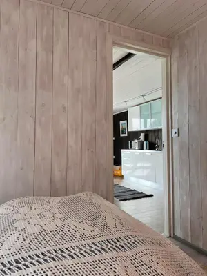 a bedroom with wooden walls and a bed and a kitchen at Yttervik gard in Steinkjer