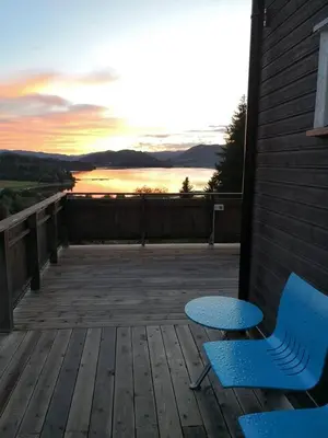 two chairs and a table on a deck with a sunset at Høgli på Yttervik gard in Fosnesstranden