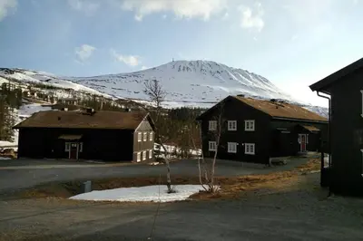 a snow covered mountain in the distance with two buildings at Apartment Gaustablikk in Gaustablikk