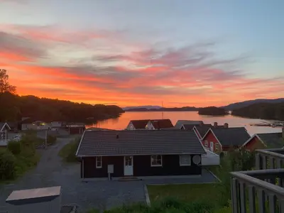 a house on the shore of a lake at sunset at Exclusive fjordside villa with swimming pool, sauna, jacuzzi and boat hire in Sveio