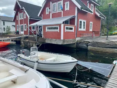 a boat is docked in front of a red house at Exclusive fjordside villa with swimming pool, sauna, jacuzzi and boat hire in Sveio
