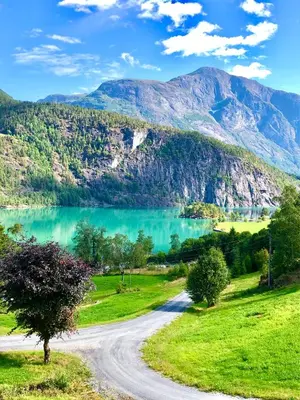 a road next to a lake with mountains in the background at Dispen feriehus in Stryn