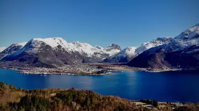 a town in the middle of a lake with snow covered mountains at Åndalsnes Sentrum 1-room Apartment in Åndalsnes