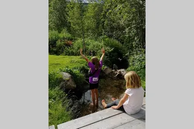 two girls sitting on a wooden bridge by a stream at Casa Kleiv i Sogndalsdalen in Sogndal