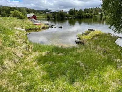 a body of water with grass and a red barn at Gammelstua ved Femund in Elga