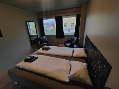 two beds in a room with two chairs and two windows at Gjøa Motell in Rosendal