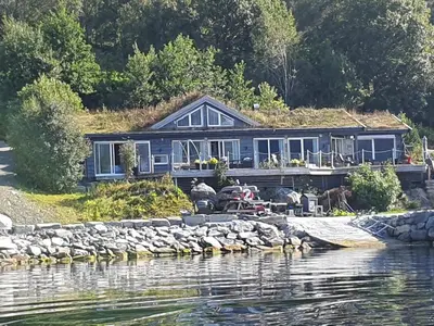 a blue house with a grass roof on the water at Småstranda Fjord Lodge in Åheim