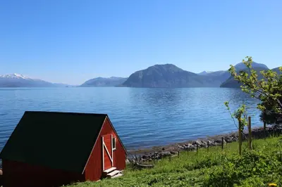a red barn sitting next to a body of water at Hjelvikhytta - flott beliggenhet ved sjøen in Hjelvik