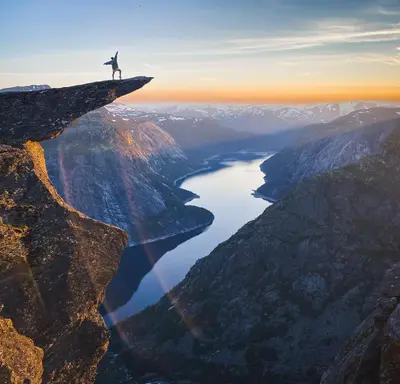 a man standing on the edge of a cliff overlooking a lake at Trolltunga Living in Tysso