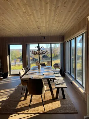 a dining room with a table and chairs and windows at Geilo - Ny og flott hytte på budalstølen in Geilo
